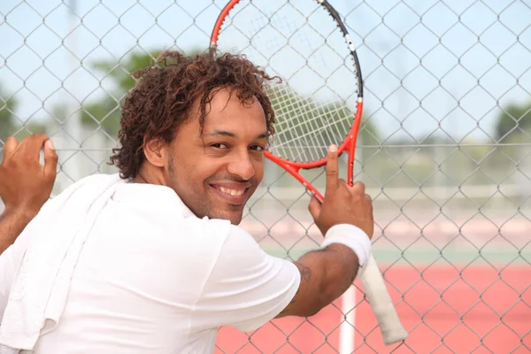 Jugador de tenis masculino apoyado en la valla de una pista dura municipal —  Fotos de Stock