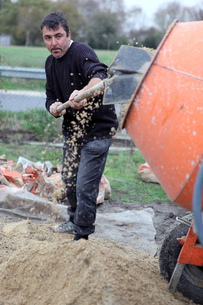 Labourer shovelling gravel into a mixer — Stock Photo, Image
