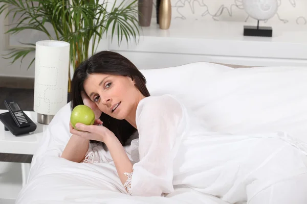 Brunetka na posteli drží jablko — Stock fotografie