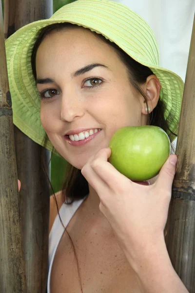 Leende kvinna med solhatt och äpple — Stockfoto