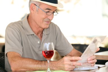 Elderly gentleman seated in cafe drinking glass of red wine clipart