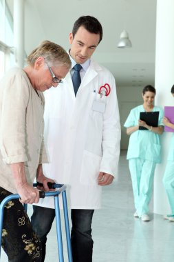 Elderly woman using a walking frame in a hospital clipart