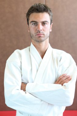 Judo practitioner standing on a mat with his arms folded clipart