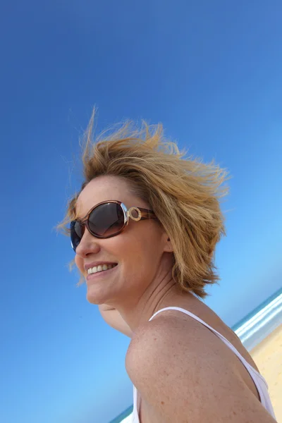Ένα χαμογελαστό γυναίκα φοράει γυαλιά ηλίου σε μια παραλία. — Φωτογραφία Αρχείου