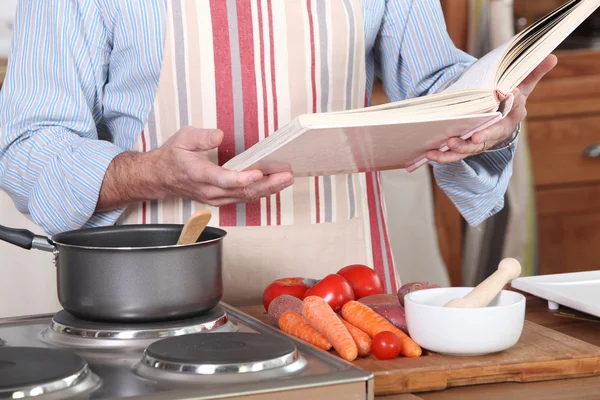 Человек, читающий книгу рецептов на кухне — стоковое фото