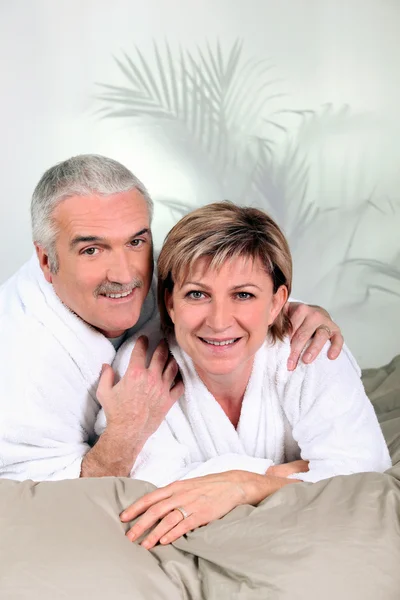 Couple mature en peignoirs de bain sur un lit — Photo