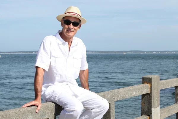 Senior en un sombrero de paja panama sentado junto al agua —  Fotos de Stock