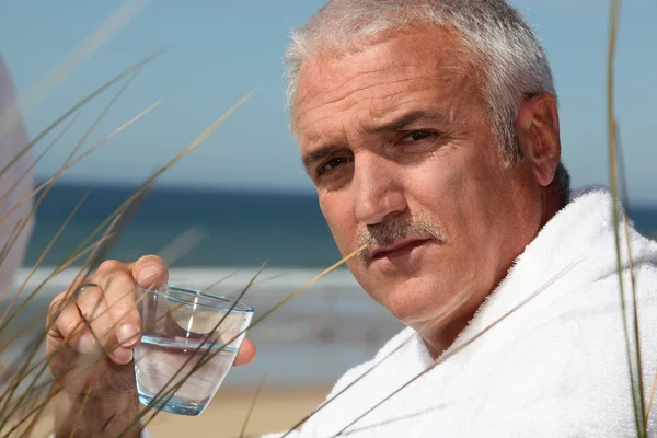 Muž seděl na pláži v županu — Stock fotografie