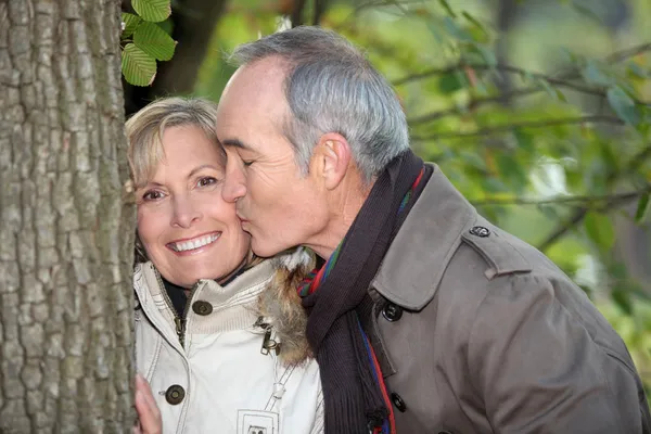 Uomo più anziano baciare il suo partner sotto un albero — Foto Stock