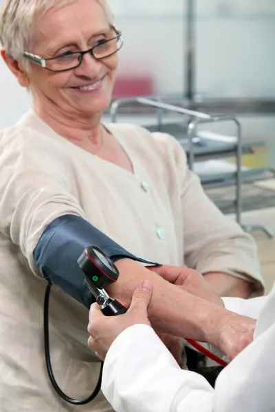 Медсестра, яка приймає кров'яний тиск усміхненої старшої жінки — стокове фото