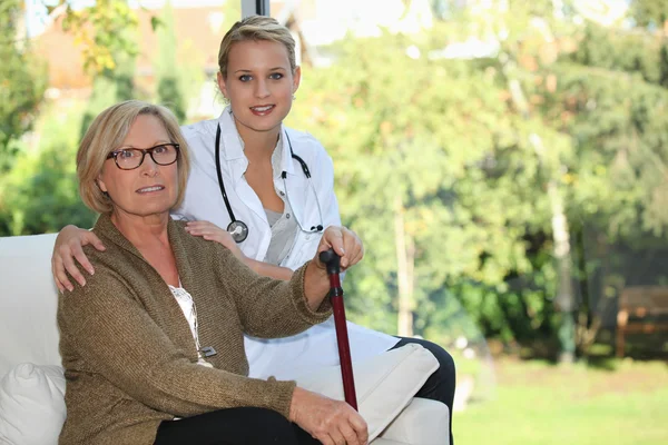 Oudere vrouw en jonge vrouwelijke verzorger thuis — Stockfoto