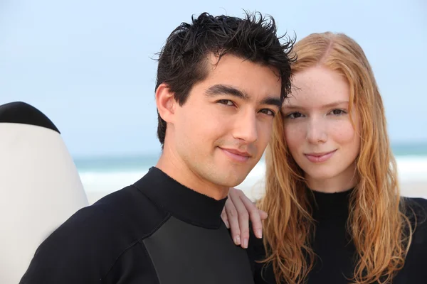 Jeune couple en combinaison à la plage — Photo