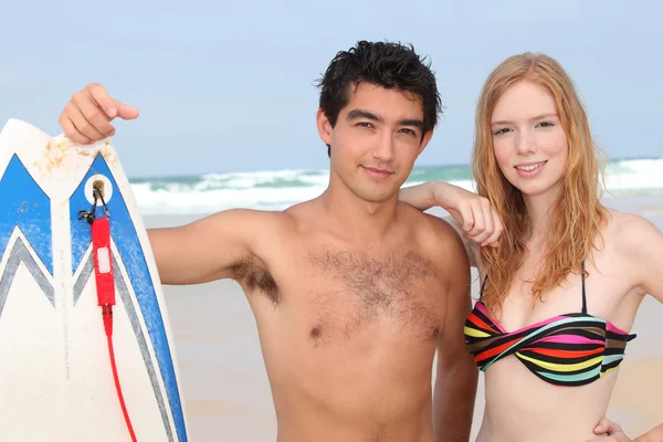 Par tonåringar poserar med surfbräda vid havet — Stockfoto