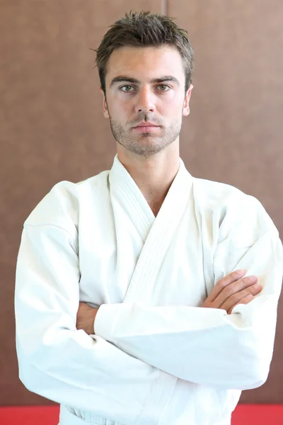Judo practitioner standing on a mat with his arms folded — Stock Photo, Image