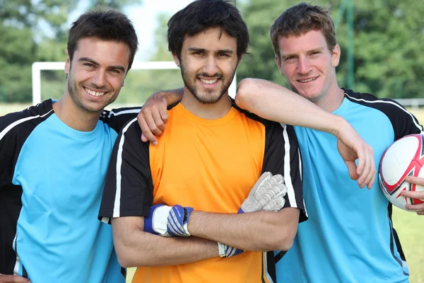 Trzy uśmiechający się piłkarze z piłką — Zdjęcie stockowe