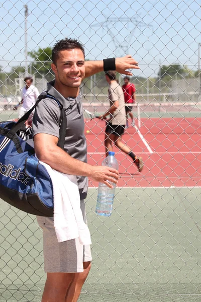 Uomo con borsa kit e bottiglia d'acqua guardare partita di tennis attraverso filo fenc — Foto Stock