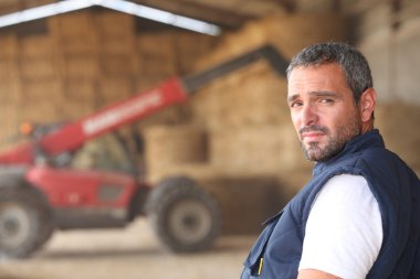 Farmer posing in front of a tractor clipart