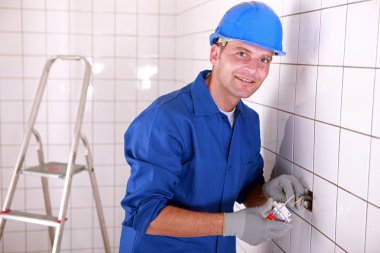 Electrician fitting a light switch in a large white tiled room clipart