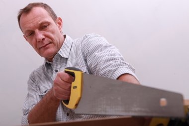 Middle-aged carpenter using hand-saw clipart