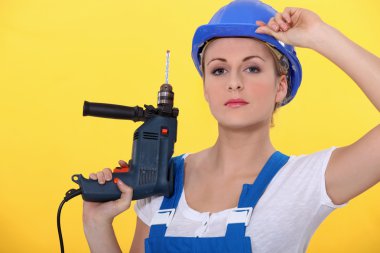 A blonde woman wearing an overall posing with a drill and adjusting her hel clipart