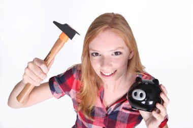 Amusing shot of young girl trying to break open her piggy bank with a hamme clipart
