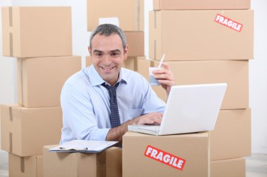 A business man drinking doing computer among cardboard boxes clipart