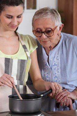 A senior woman looking a young woman cooking clipart