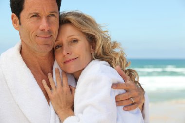 Couple embracing by the sea in toweling robes clipart