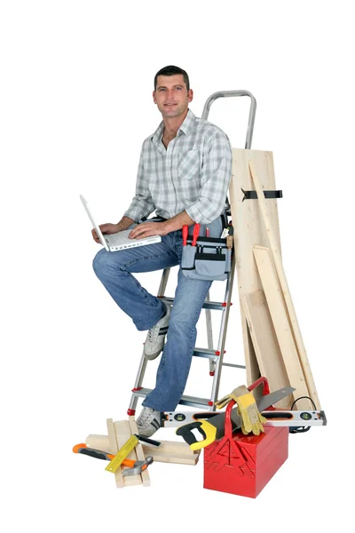 Handyman sentado em uma escada com laptop — Fotografia de Stock