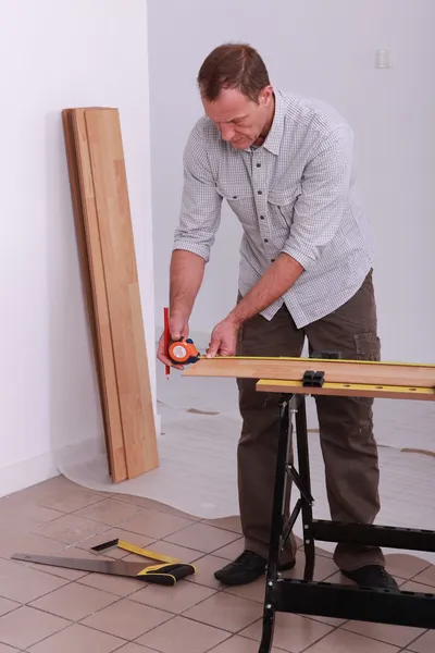 Handyman medindo uma placa de madeira com uma fita métrica — Fotografia de Stock