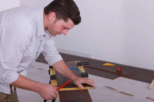 Чоловік кладе підлогу і вимірює шматок деревини — стокове фото