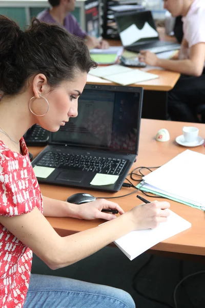 Vrouw in een drukke kantoor werken op een laptop — Stockfoto