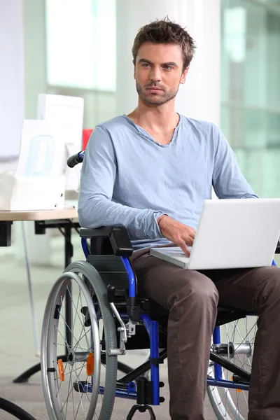 坐在轮椅上用的笔记本电脑的雇员 — 图库照片
