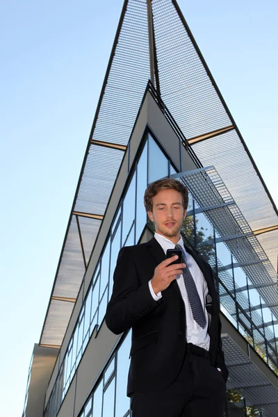 Молодой человек с мобильным телефоном перед современным зданием — стоковое фото