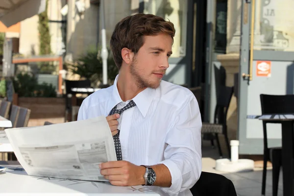 Молодой человек за столиком кафе читает газету — стоковое фото