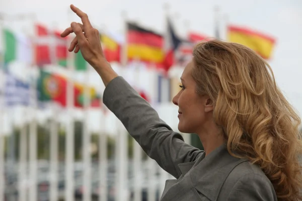 Woman hailing a taxi in front of international flags — Stock Photo, Image