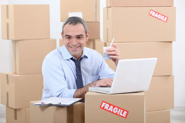 A business man drinking doing computer among cardboard boxes — Stock Photo, Image