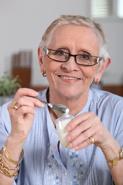 Счастливая пожилая женщина ест йогурт — стоковое фото