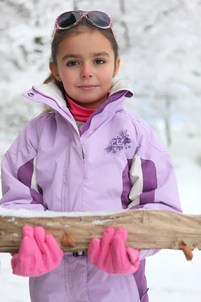 Little girl carrying a log through the snow — Stock Photo, Image