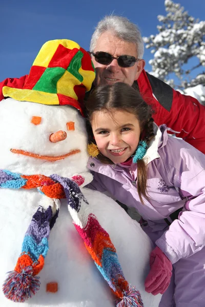 Portrait of a senior man and a little girl with snowman — Stock Photo, Image