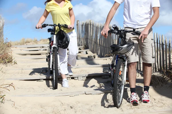 Ung man och kvinna ridning cyklar på stranden — Stockfoto