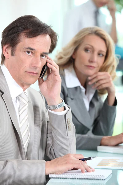 Un hombre de negocios usando un teléfono móvil y siendo observado por una mujer de negocios du —  Fotos de Stock