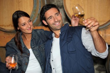 Smiling man and woman tasting wine in a cellar clipart