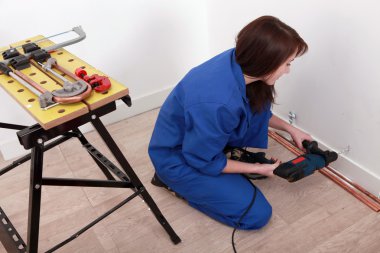 Female plumber installing hot and cold water pipes clipart