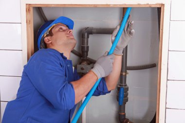 Plumber feeding blue flexible pipe behind a tiled wall clipart