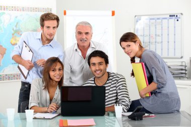 Young team of sitting around a laptop with an older guy clipart