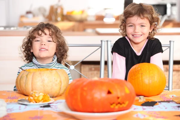 Little boy and girl dressed in pajamas posing behind pumpkins — Stock Photo, Image