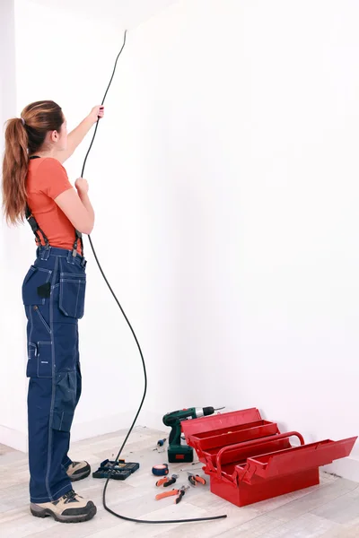 Eletricista feminino puxando cabo através da parede — Fotografia de Stock