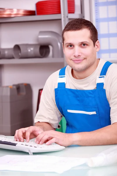 Young plumber typing at a computer — Stock Photo, Image