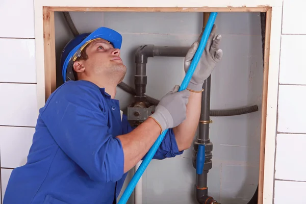 Водопроводчик подает голубую гибкую трубу за плиточной стеной — стоковое фото